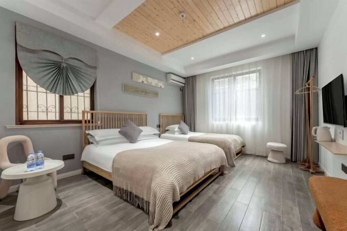 Ein Hotelzimmer mit zwei Betten, einem kleinen Tisch mit Wasserflaschen, einem Fernseher und einer Holzbalkendecke.