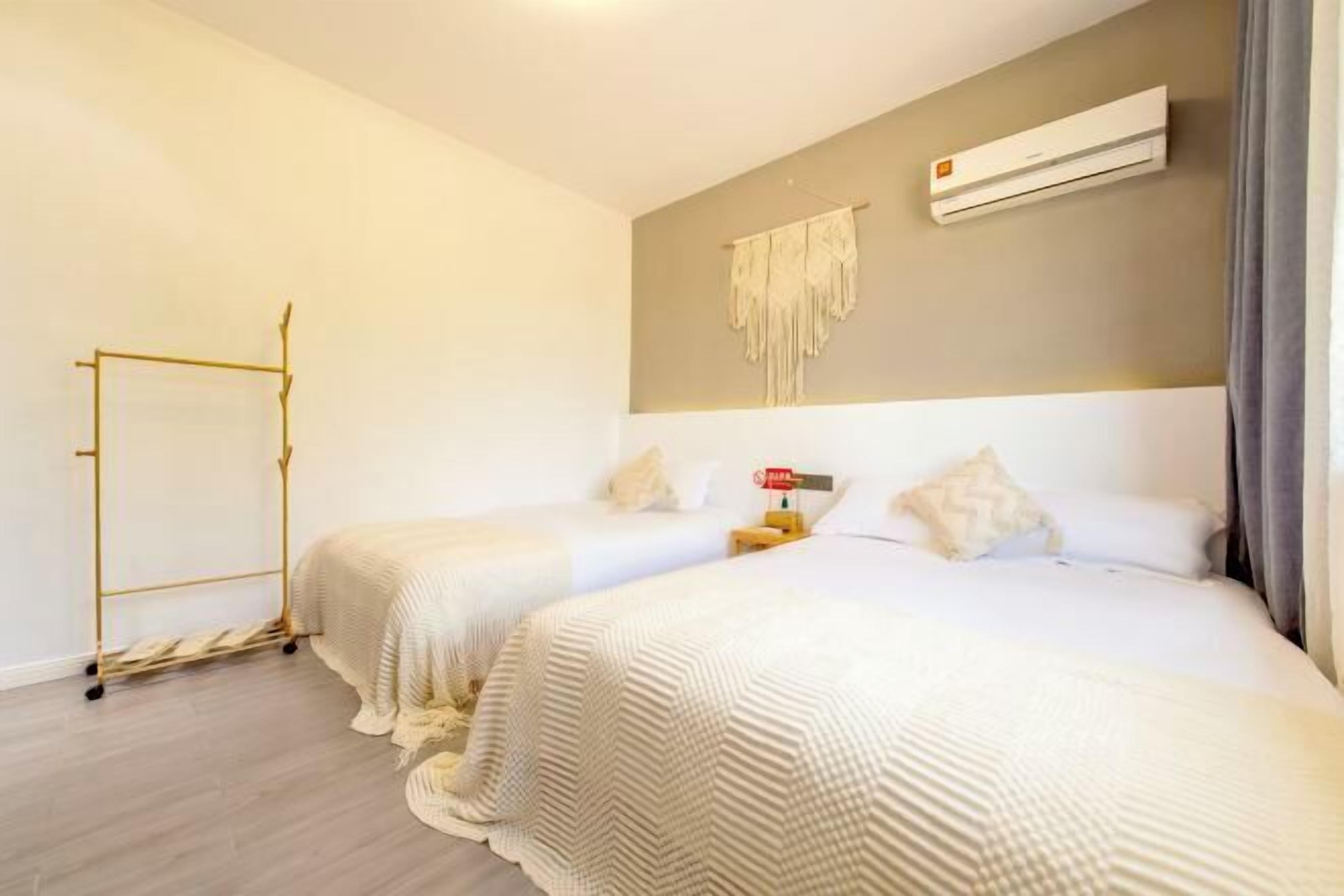 Habitación de hotel con dos camas, un armario, un equipo de aire acondicionado e iluminación en la pared.