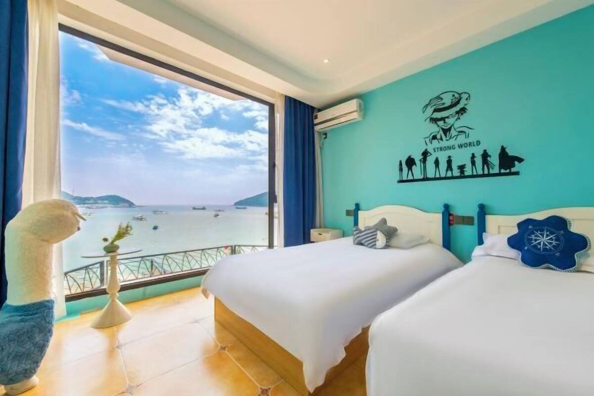 Ein Hotelzimmer mit zwei Betten, einem großen Fenster mit Meerblick und einer Wanddekoration.