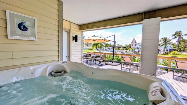 A hot tub with a view of a patio area, a framed picture on the wall, and a clear sky.