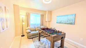 A room with a foosball table, a sofa, a lamp, and a painting on the wall.