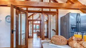 A kitchen with a wooden ceiling, a refrigerator, and a breakfast setup with bread and orange juice.