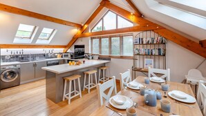A modern kitchen with a central island, wooden beams, and a dining area with a table set for four.
