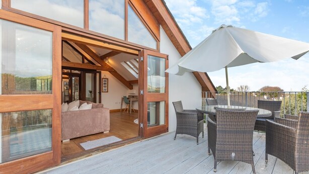 A modern house with a large glass door leading to a living area with a sofa and a dining table with chairs.