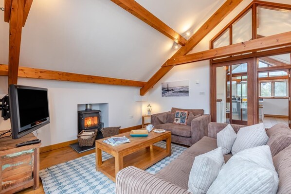 Ein gemütliches Wohnzimmer mit Kamin, Holzbalken, einem Fernseher und einer Couch.