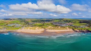 An aerial view of a coastal town with a beach, green fields, and a mix of residential and commercial buildings.