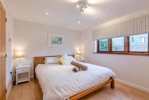 Ein Schlafzimmer mit einem hölzernen Bett, weißer Bettwäsche, zwei Nachttischlampen, einem Nachttisch, einem Fenster mit Aussicht und einer Deckenleuchte.
