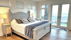A bedroom with a large bed, wooden flooring, a nightstand with a lamp, and a view of the outdoors through a door. - NEW "Seabreeze B&B" on walkout beach in beautiful Qualicum Beach (Qualicum Beach)