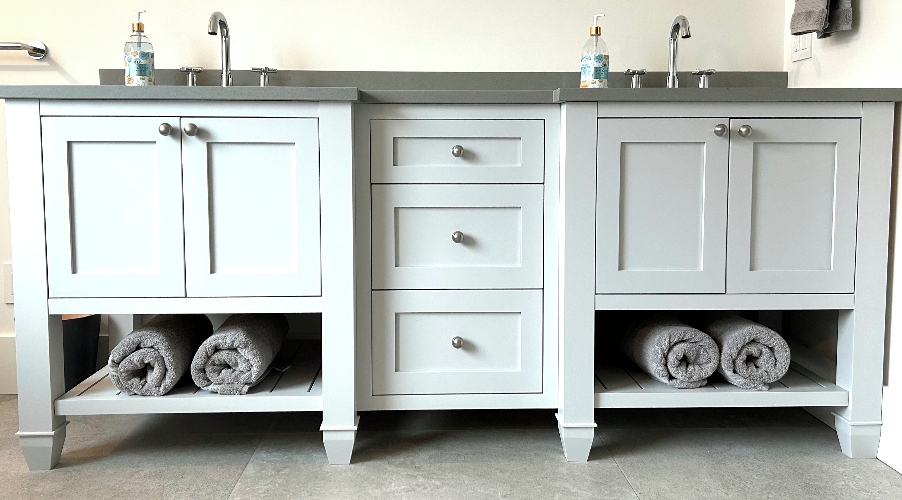 A bathroom with a white vanity, two sinks, and three drawers.