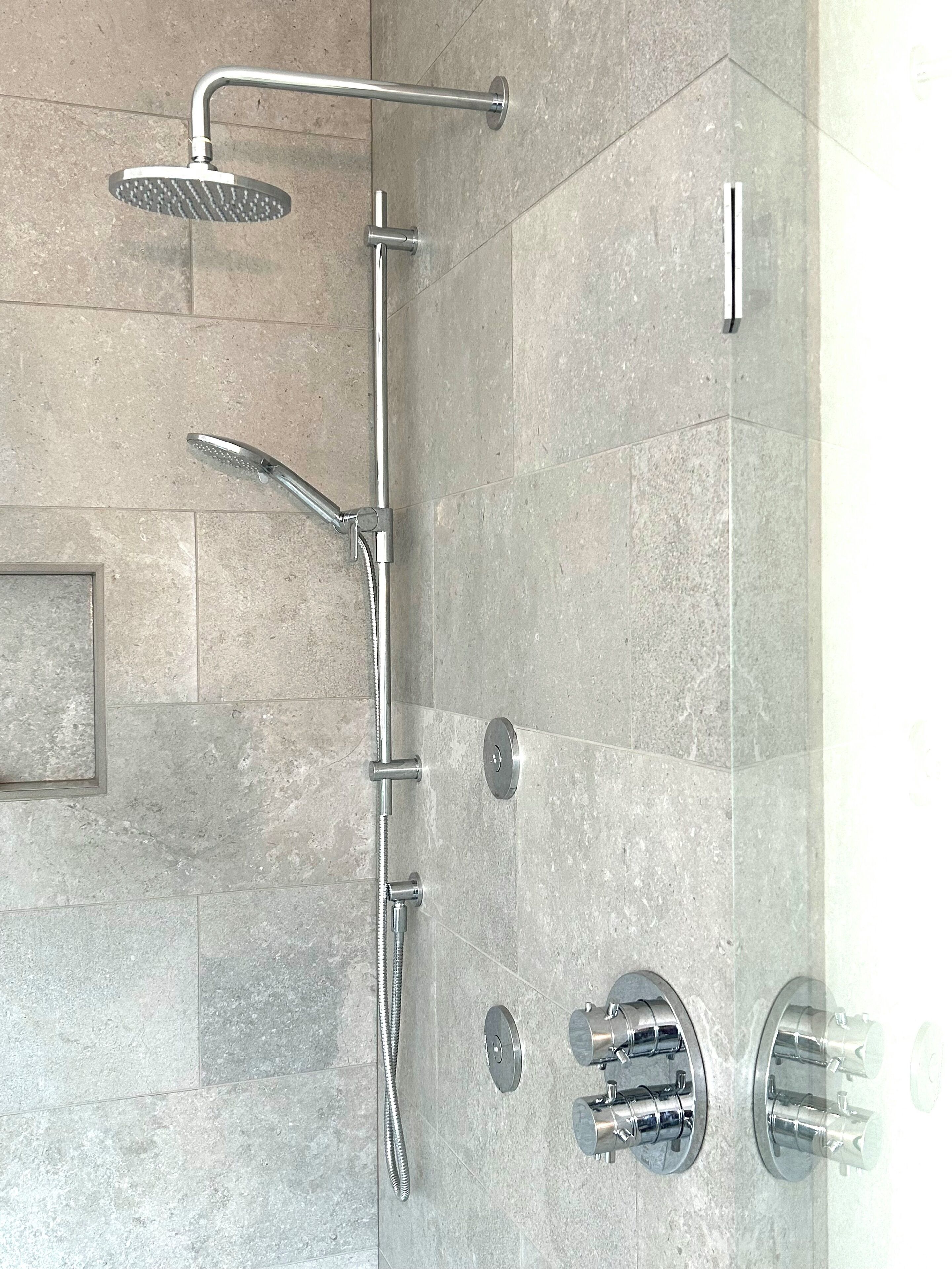Una ducha moderna con múltiples cabezales y zona de ducha con cerramiento de vidrio.