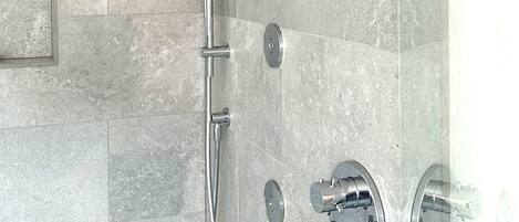 Una ducha moderna con múltiples cabezales y zona de ducha con cerramiento de vidrio.