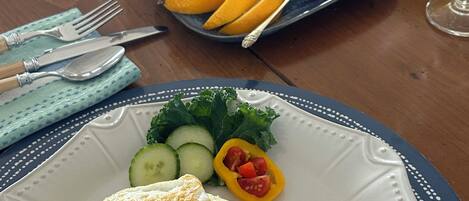 A breakfast setting with a plate of toast topped with avocado and egg, a side salad, and a plate of fruit including kiwi and orange slices.