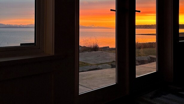 A view from inside a building with large windows overlooking a sunset over a body of water. - NEW "Seabreeze B&B" on walkout beach in beautiful Qualicum Beach (Qualicum Beach)