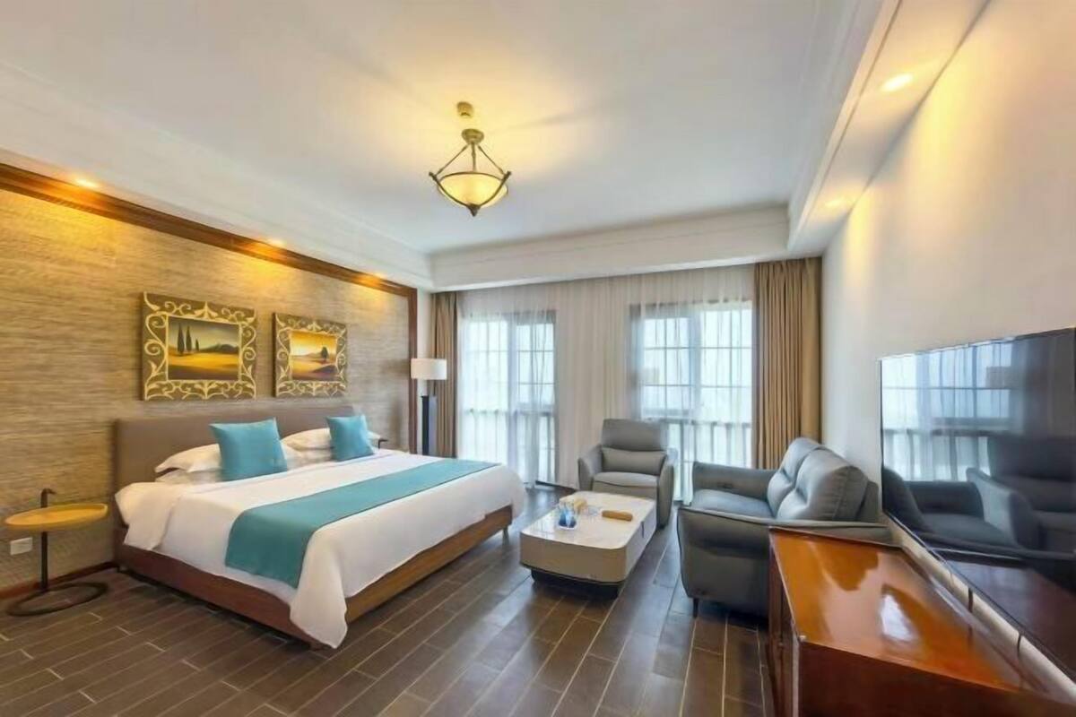 A hotel room with a bed, a coffee table, a sofa, a TV, and two paintings on the wall.