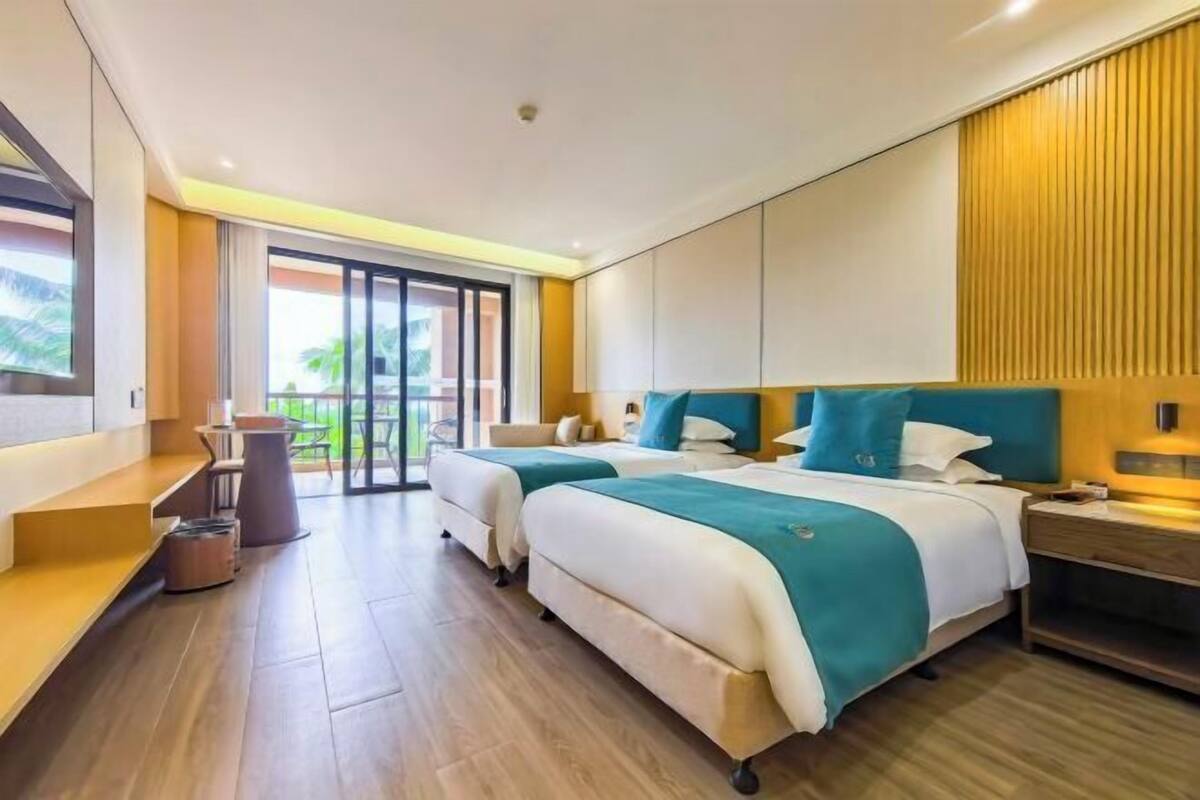A hotel room with two beds, a desk, and a view of palm trees.
