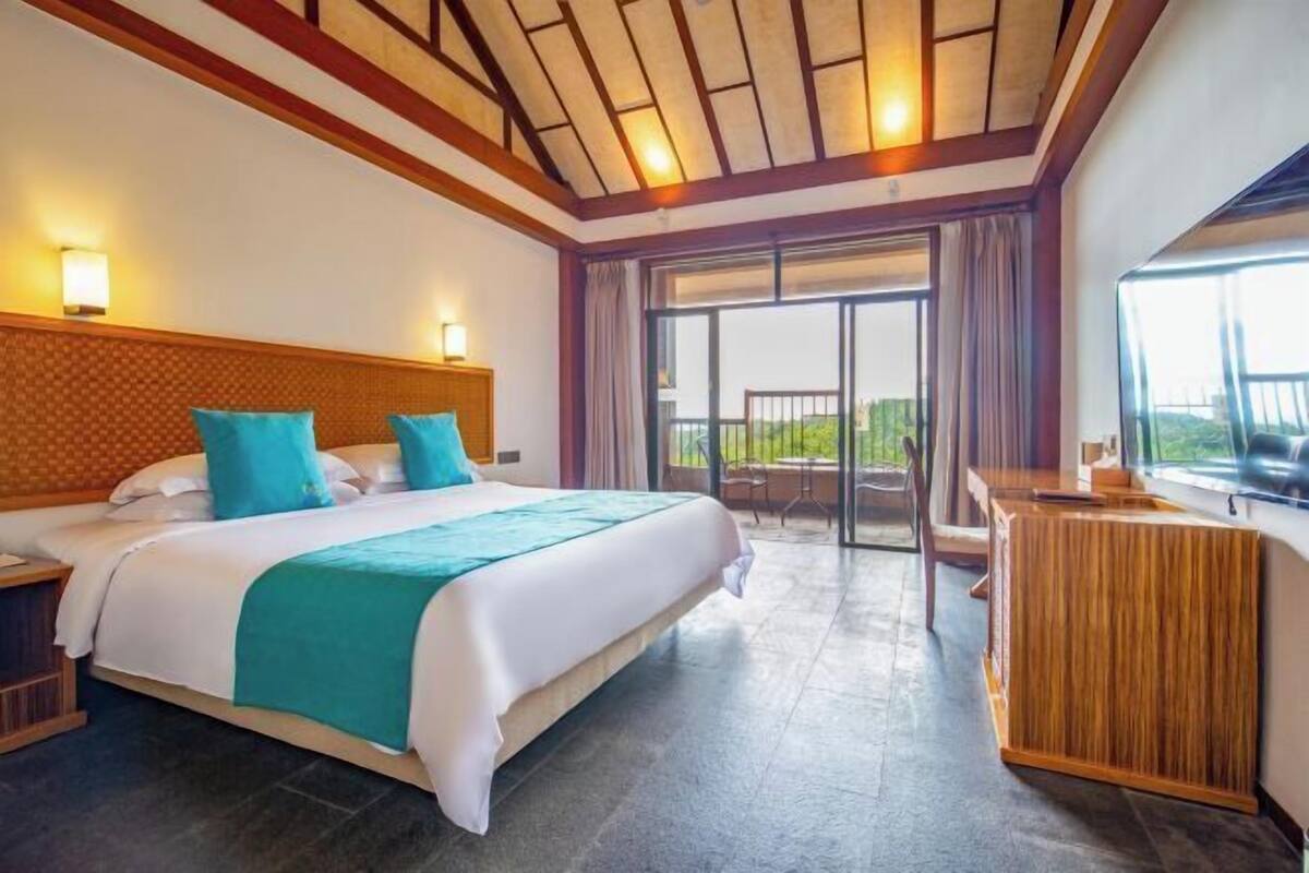 A hotel room with a large bed, a wooden headboard, a balcony with a view, and a wooden desk.