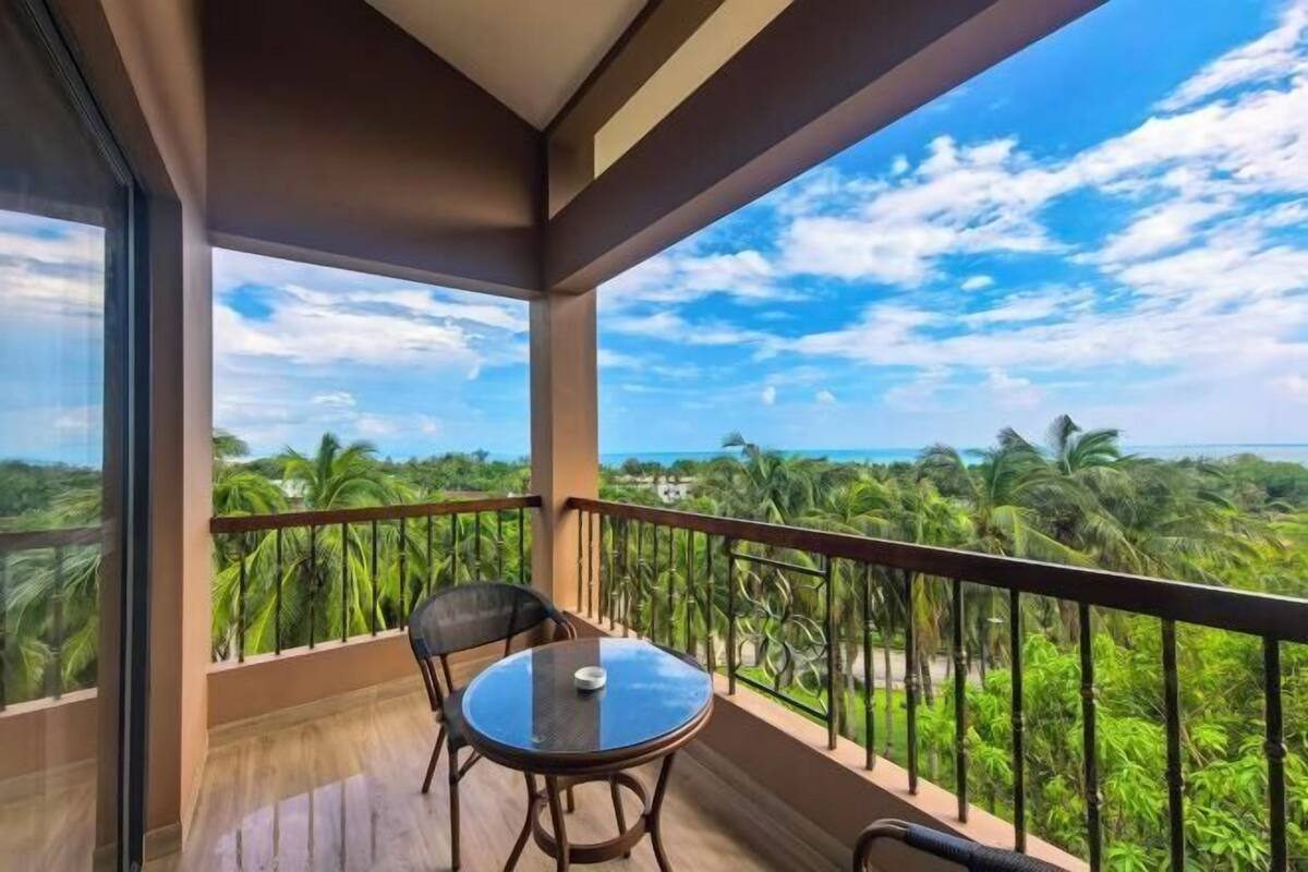 A balcony with a table and chairs, overlooking a tropical landscape with palm trees and a clear sky.