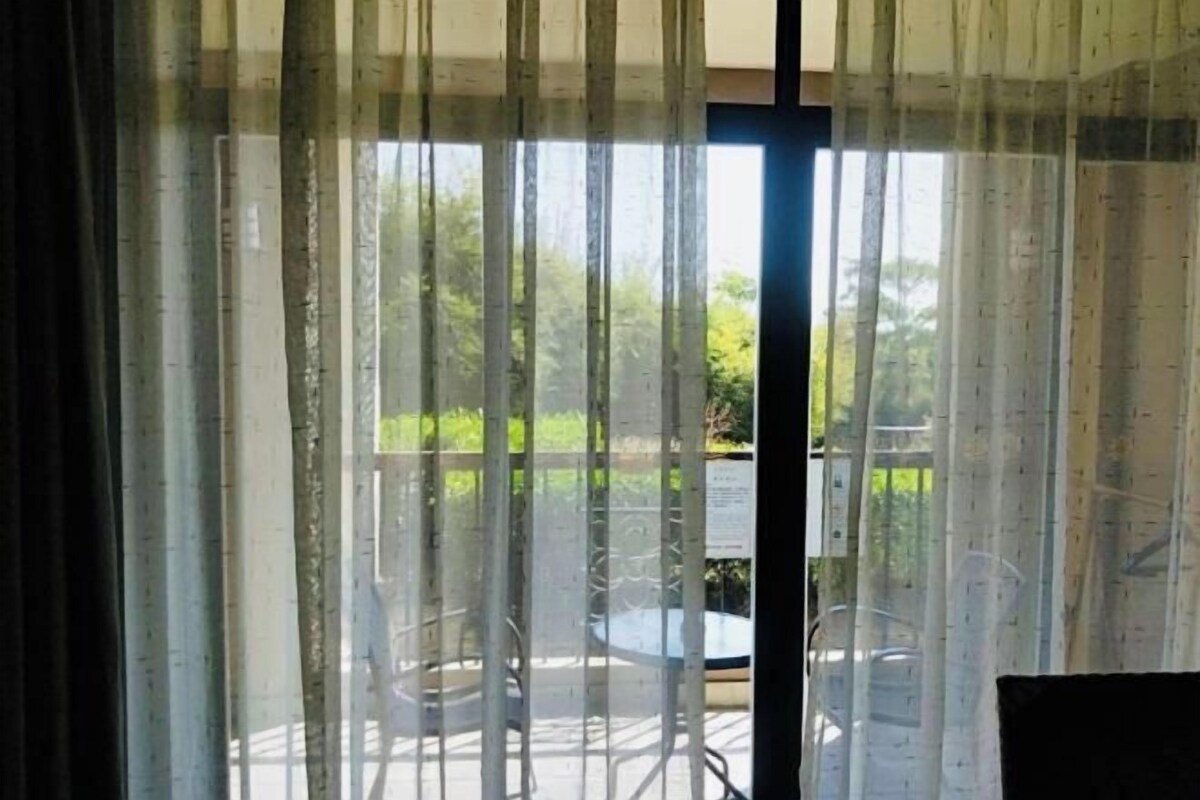 A room with a view through sheer curtains to an outdoor area with a table and chairs.