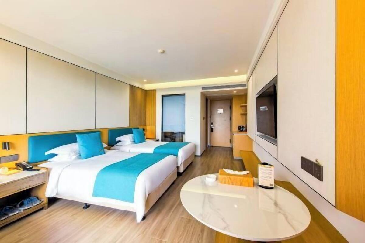 A hotel room with two beds, a TV, a small table, and a shoe rack.