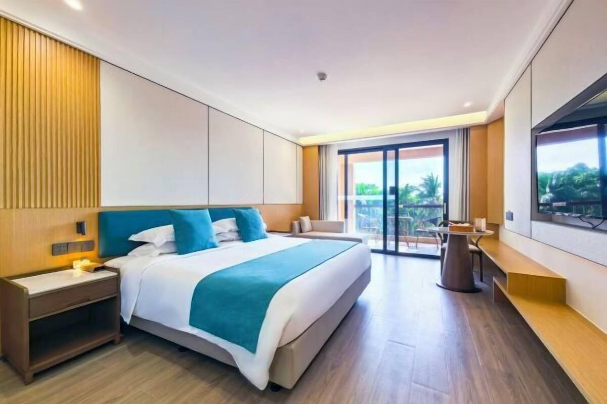 A modern hotel room with a large bed, a desk, and a balcony with a view.