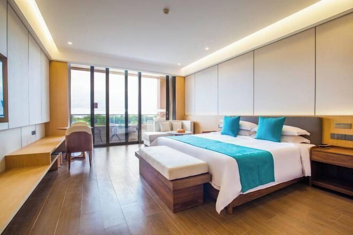 A modern hotel room with a large bed, a seating area, and a balcony with a view.