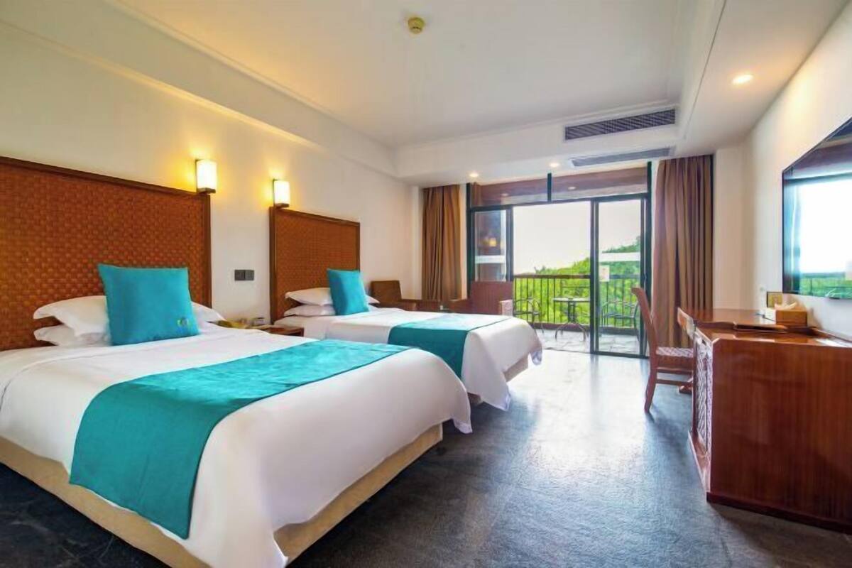 A hotel room with two beds, a desk, and a balcony with a view.