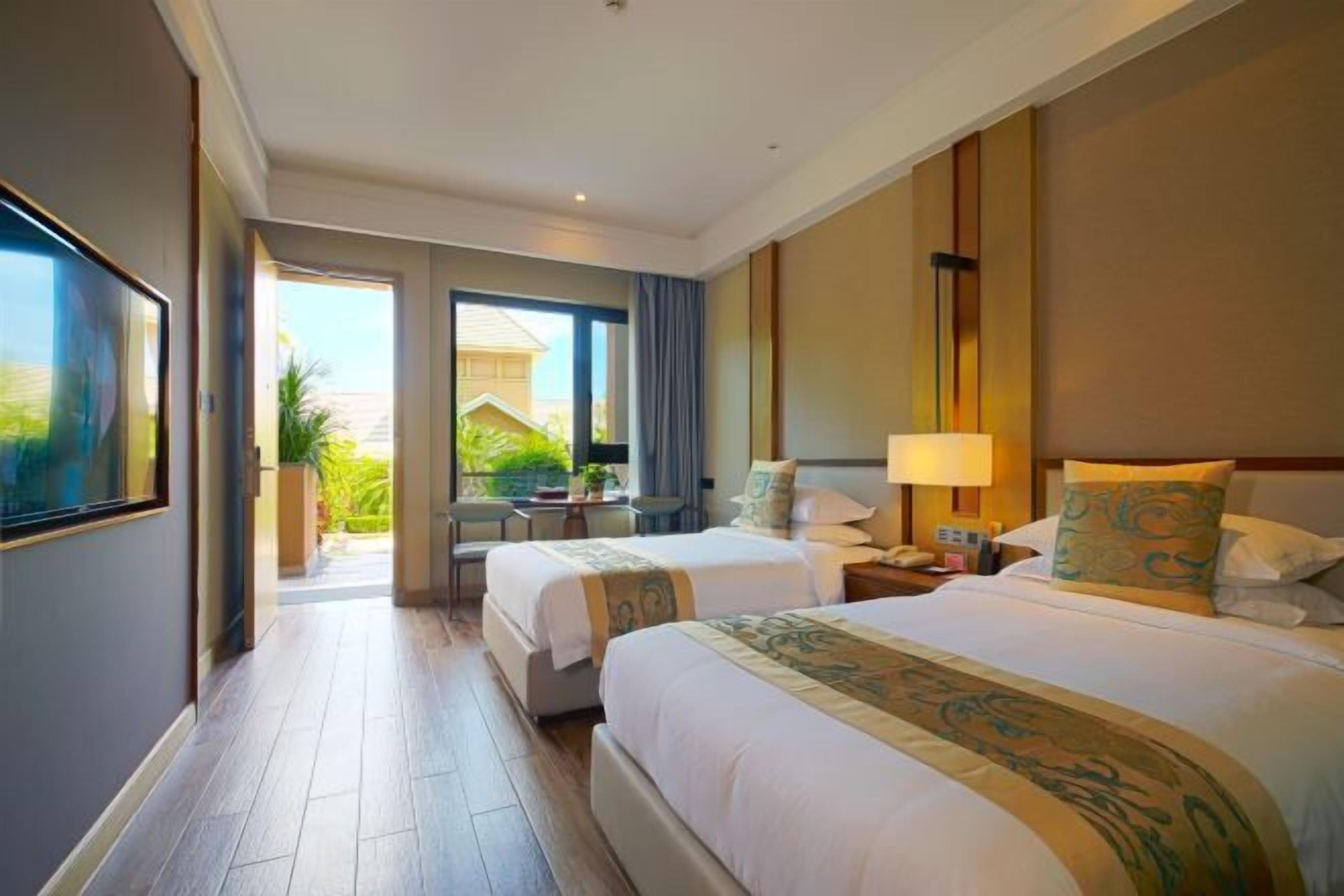 A hotel room with two beds, a desk, a chair, and a view of the outside.