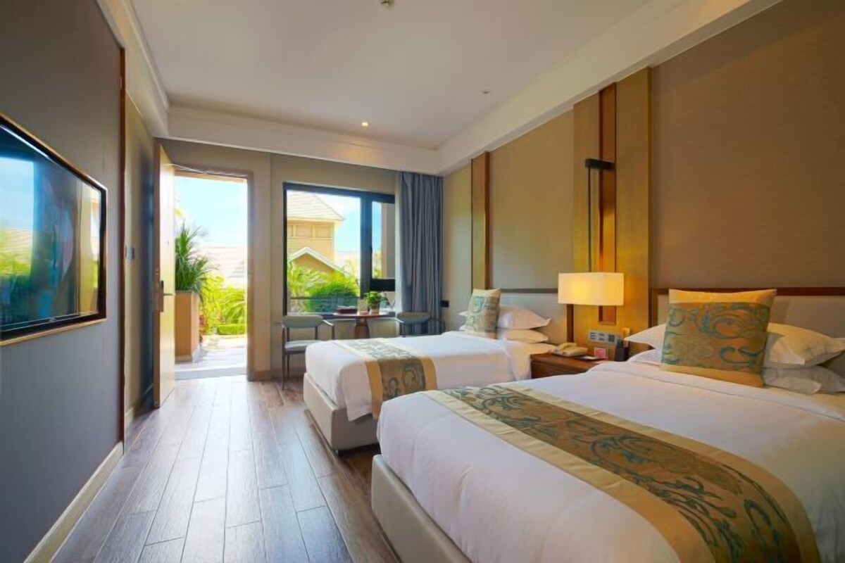 A hotel room with two beds, a desk, a chair, and a view of the outside.