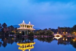 A traditional pavilion with a reflection in the water, surrounded by palm trees and rocks. - Nanshan Hotel (Sanya)