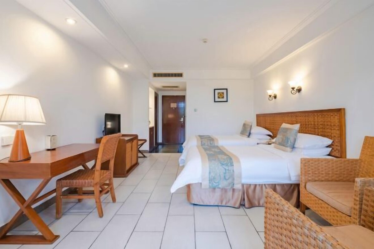 A hotel room with a bed, a desk, a chair, and a lamp.