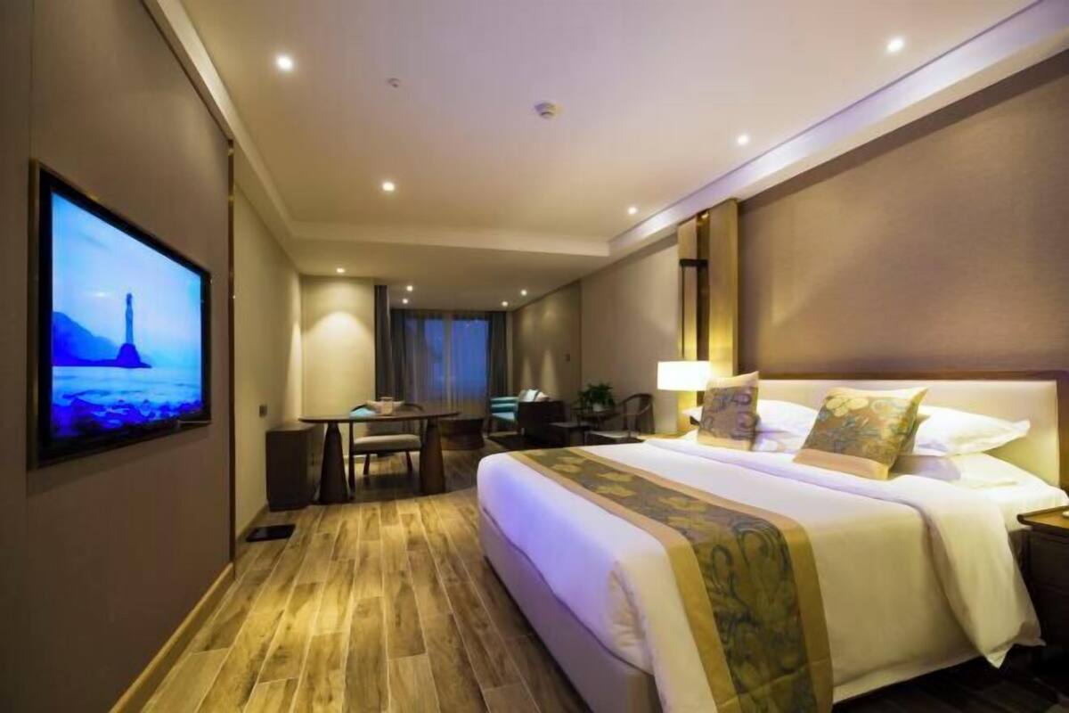 A hotel room with a large bed, a desk, a chair, a TV, and a lamp.