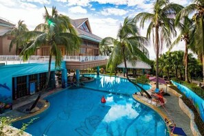 Piscina cercada por palmeiras e um edifício ao fundo.