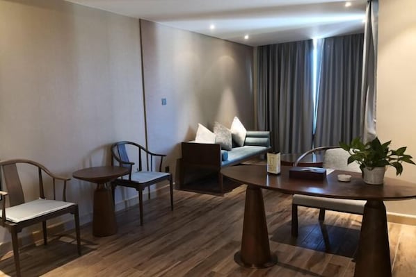 Ett modernt hotellrum med trägolv, ett runt matbord, två stolar, en soffa och ett stort fönster med gardiner.