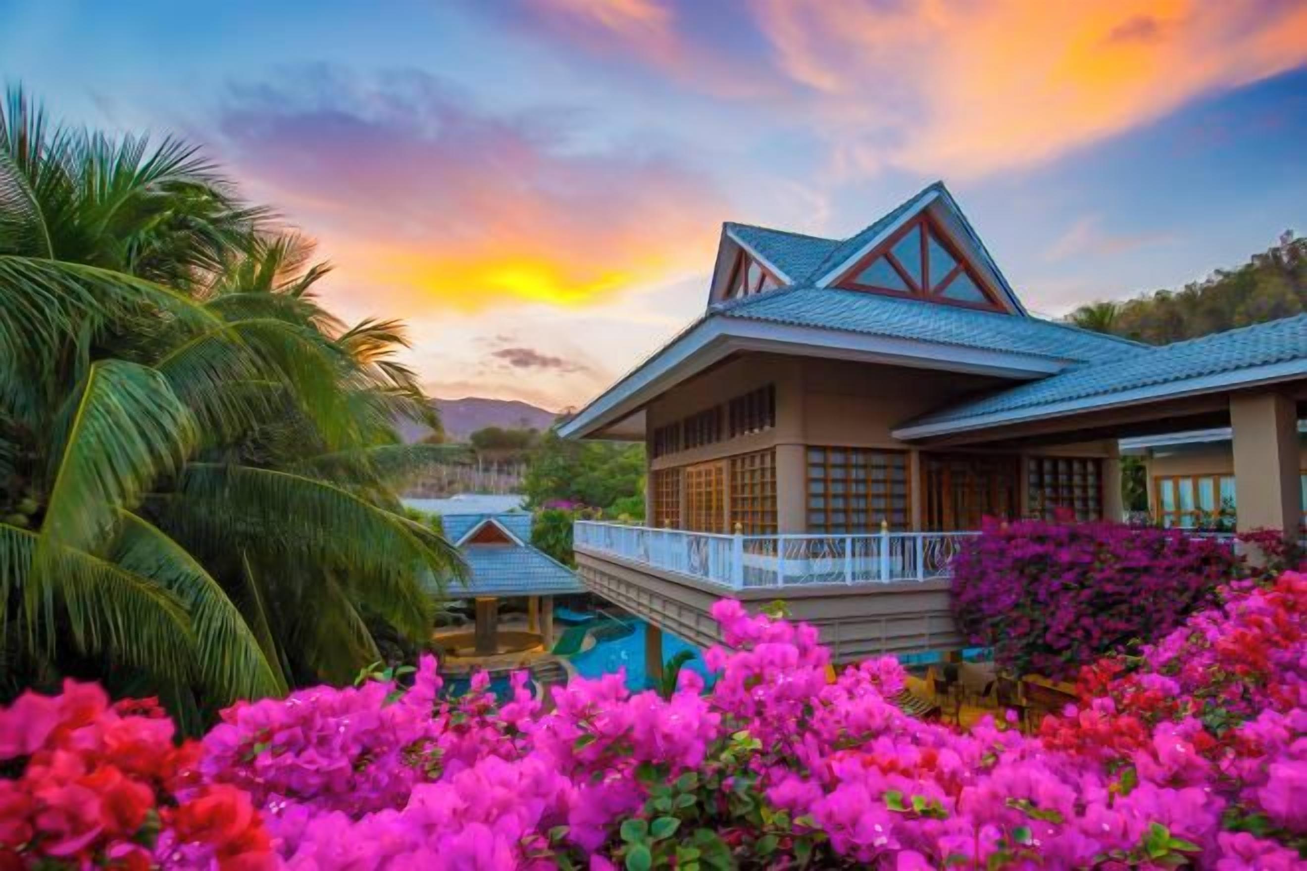 A house with a balcony, surrounded by lush greenery and vibrant flowers.