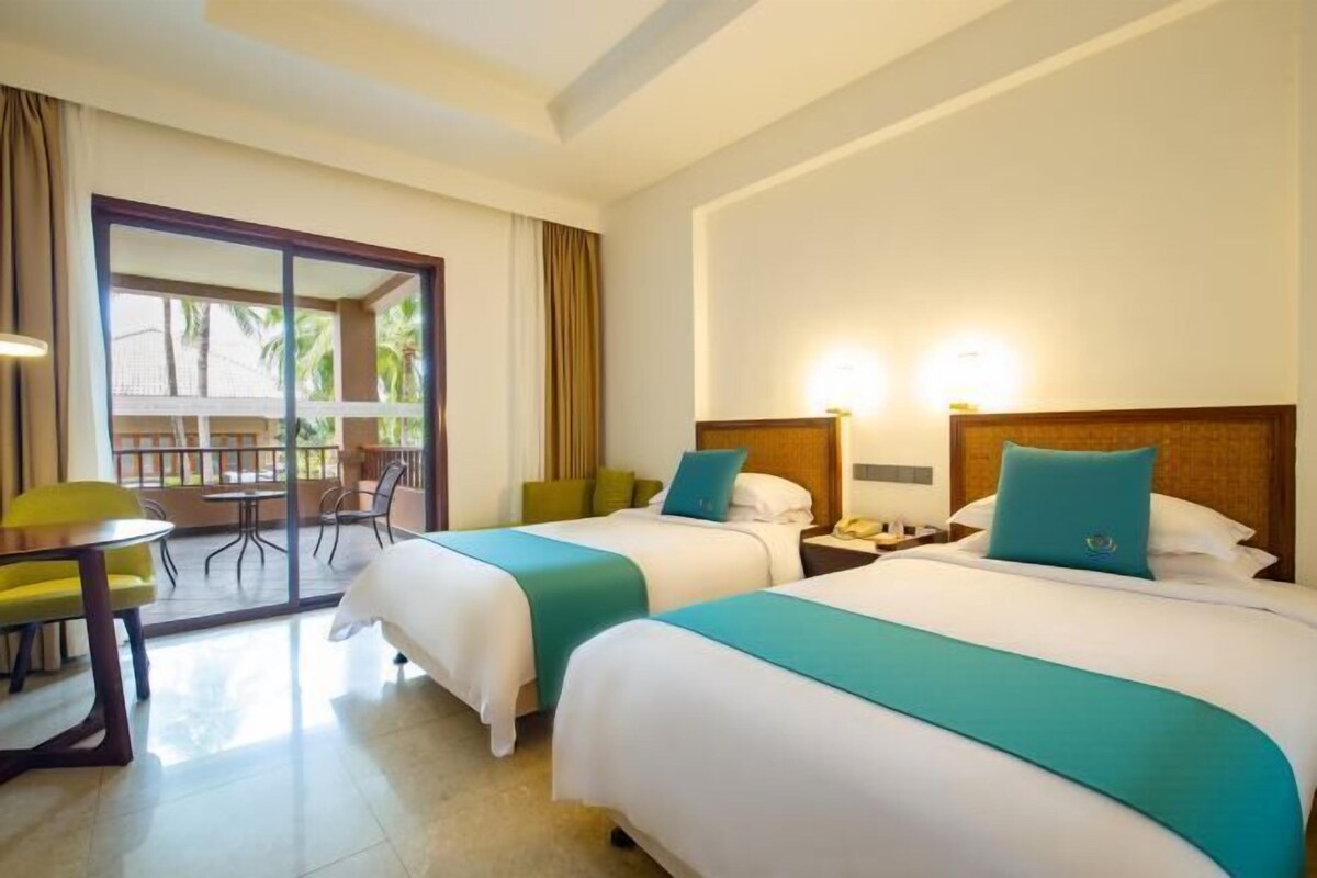 A hotel room with two beds, a balcony, a desk, and a chair.