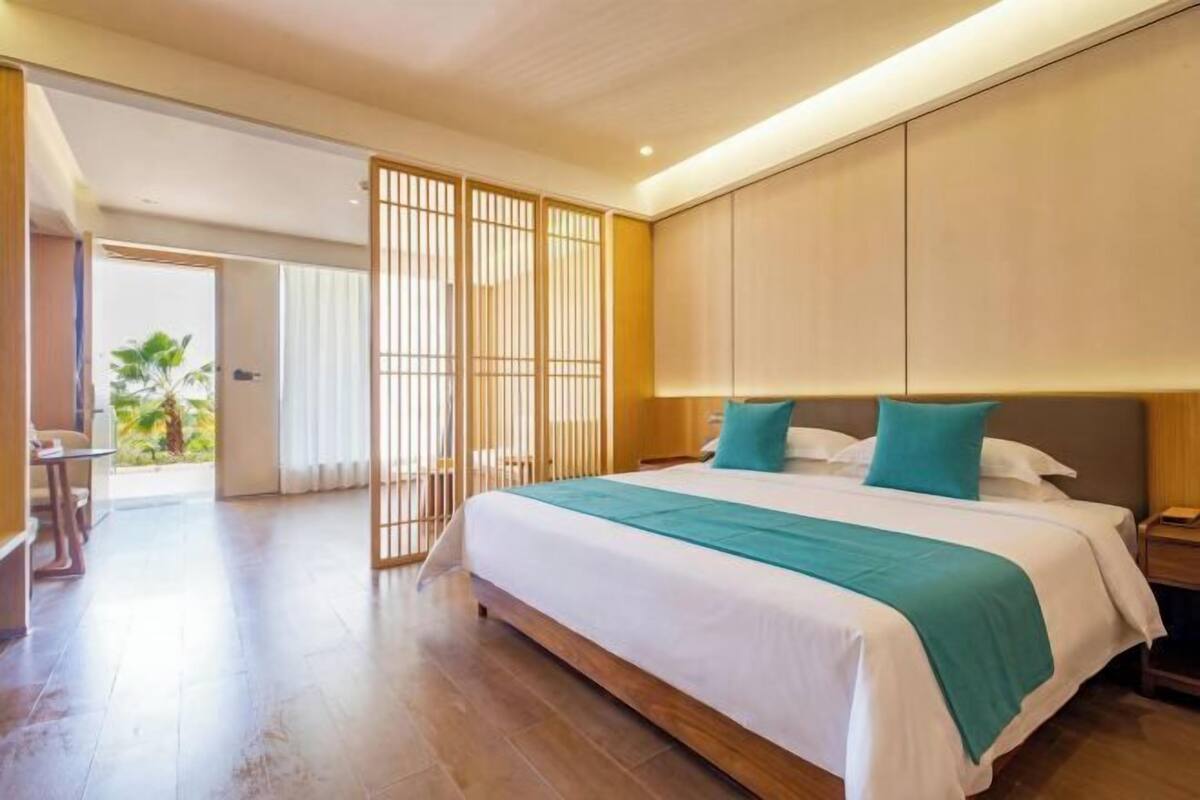 A hotel room with a bed, bedside table, and a view of the outdoors.