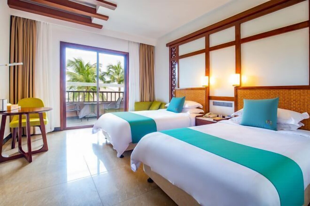 A hotel room with two beds, a balcony, a dining area, and a view of palm trees.