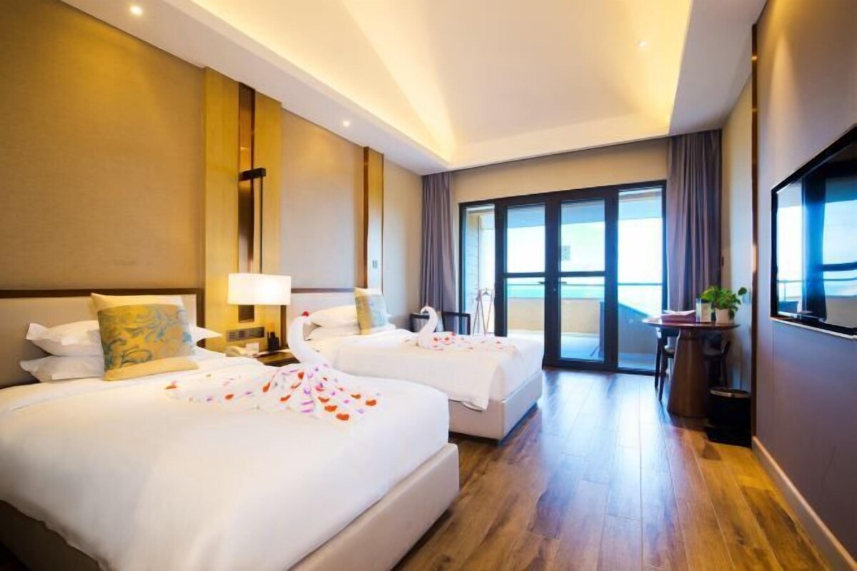 A hotel room with two beds, a balcony, a desk, and a large window.