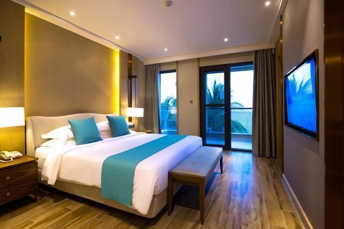 A hotel room with a large bed, a bench, a TV, and a balcony with a view.