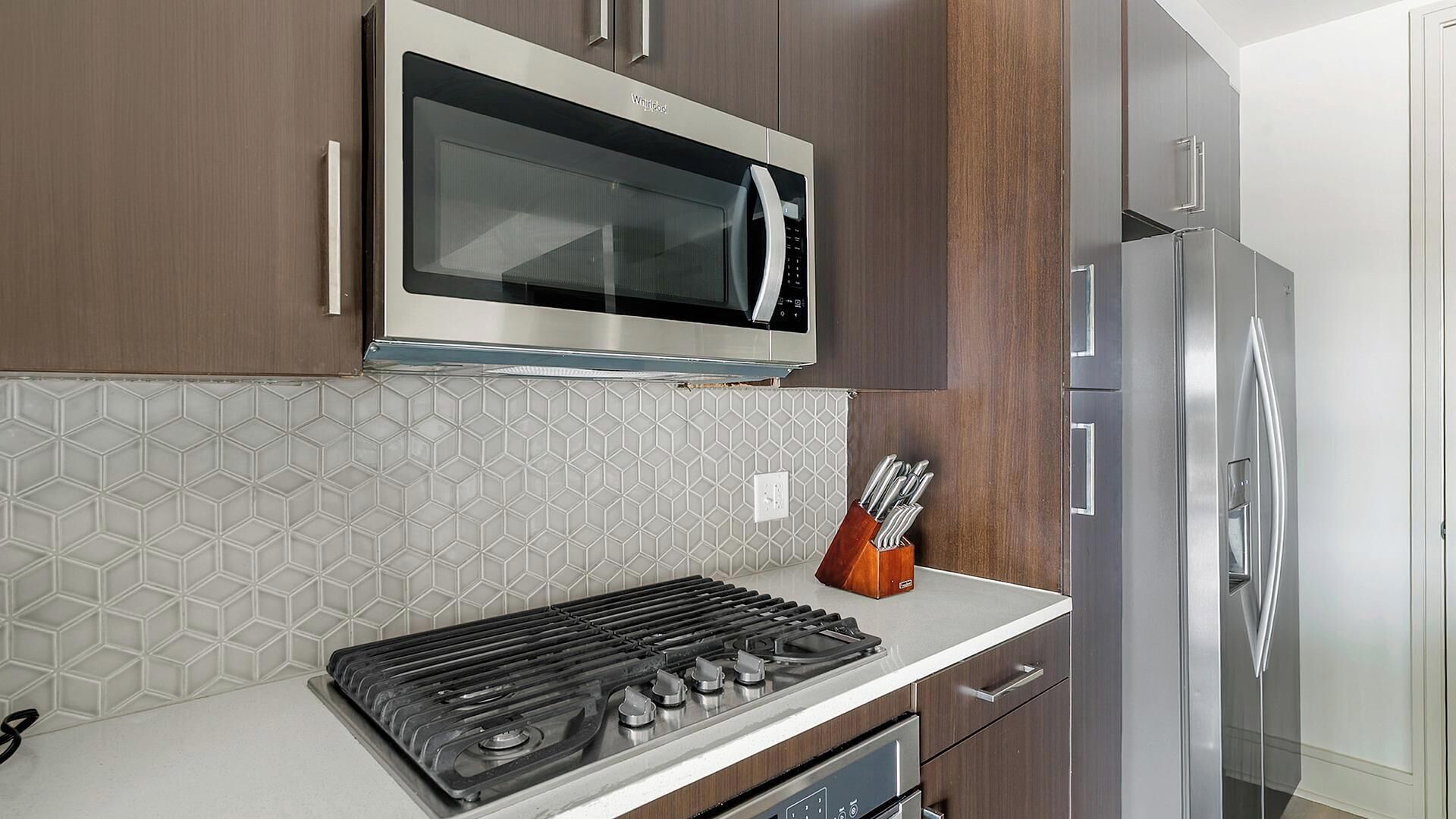 A modern kitchen with a stainless steel microwave, gas stove, and a refrigerator.