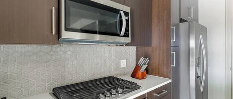 A modern kitchen with a stainless steel microwave, gas stove, and a refrigerator.