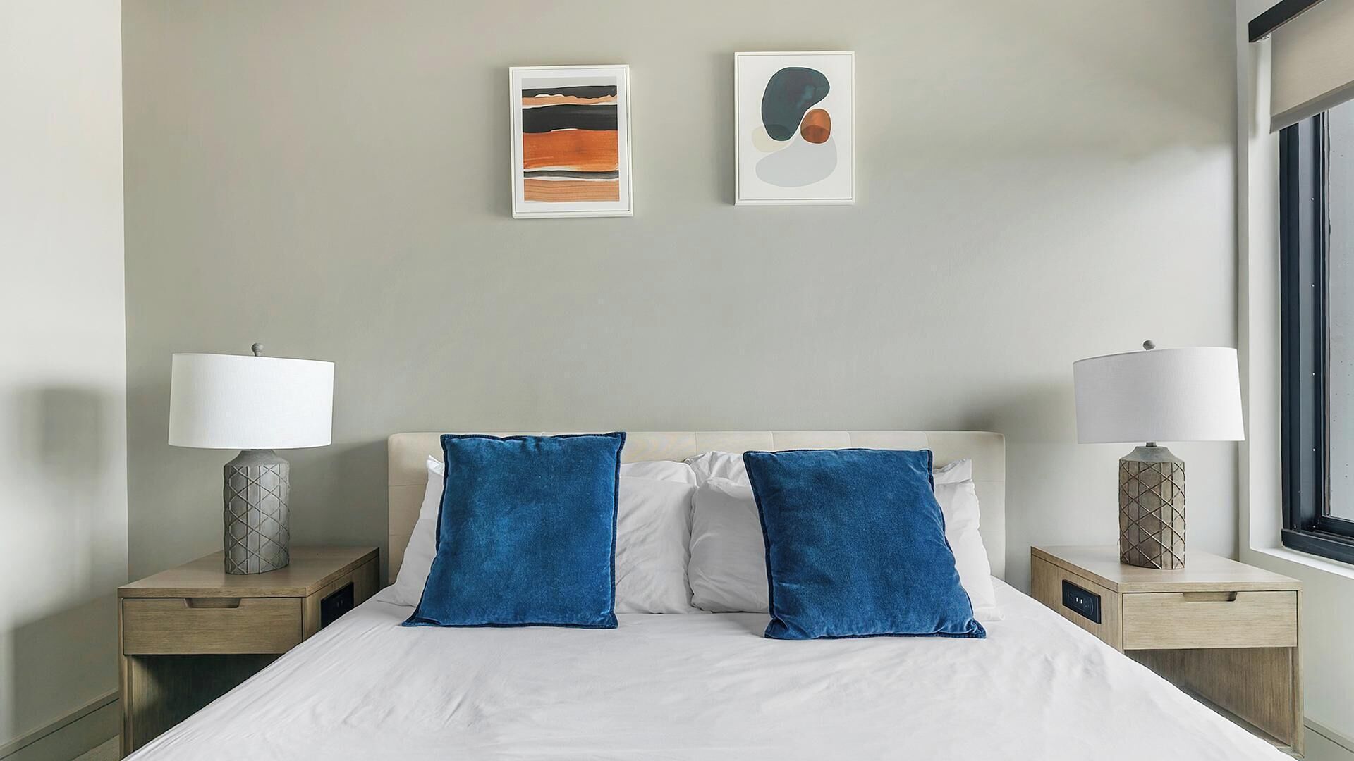 A hotel room with a bed, two nightstands, two lamps, and two wall art pieces.