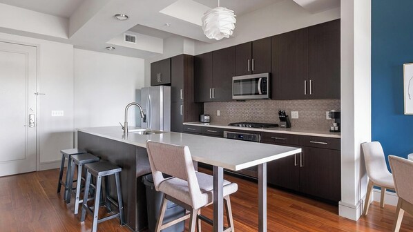 Una cocina moderna con armarios oscuros, electrodomésticos de acero inoxidable y una isla central con taburetes de bar.