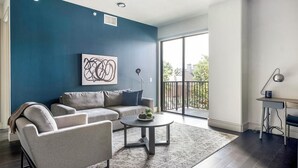 A modern living room with a blue accent wall, a gray sofa, a coffee table, and a view of the outdoors through a large sliding glass door.