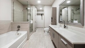 A modern bathroom with a bathtub, a shower, a toilet, and a vanity with a mirror. - Landing | Stylish 2BD, Courtyard, Gym (Houston)