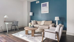 A living room with a blue accent wall, a beige sofa, two side tables with lamps, a coffee table, and a gray chair.