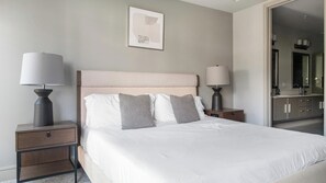 A hotel room with a bed, two bedside tables, a nightstand, a mirror, and a wall-mounted artwork.