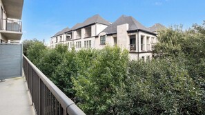 A multi-story residential building with a balcony and a view of dense greenery.