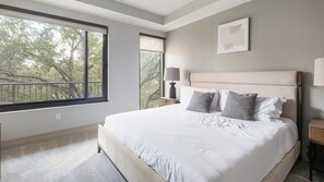 A bedroom with a large window, a bed with white bedding, and a nightstand with a lamp. - Landing | Beautiful 2BD, Pool, Gym (Houston)