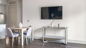 A modern kitchen with a dining area, a flat-screen TV mounted on the wall, and a small table with a vase.